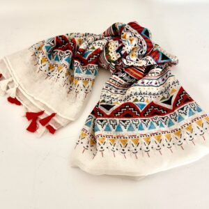 Lightweight cream scarf printed with bands of geometric patterns in terracotta red, turquoise, mustard yellow and black, finished with alternating red and white tassels along the ends.