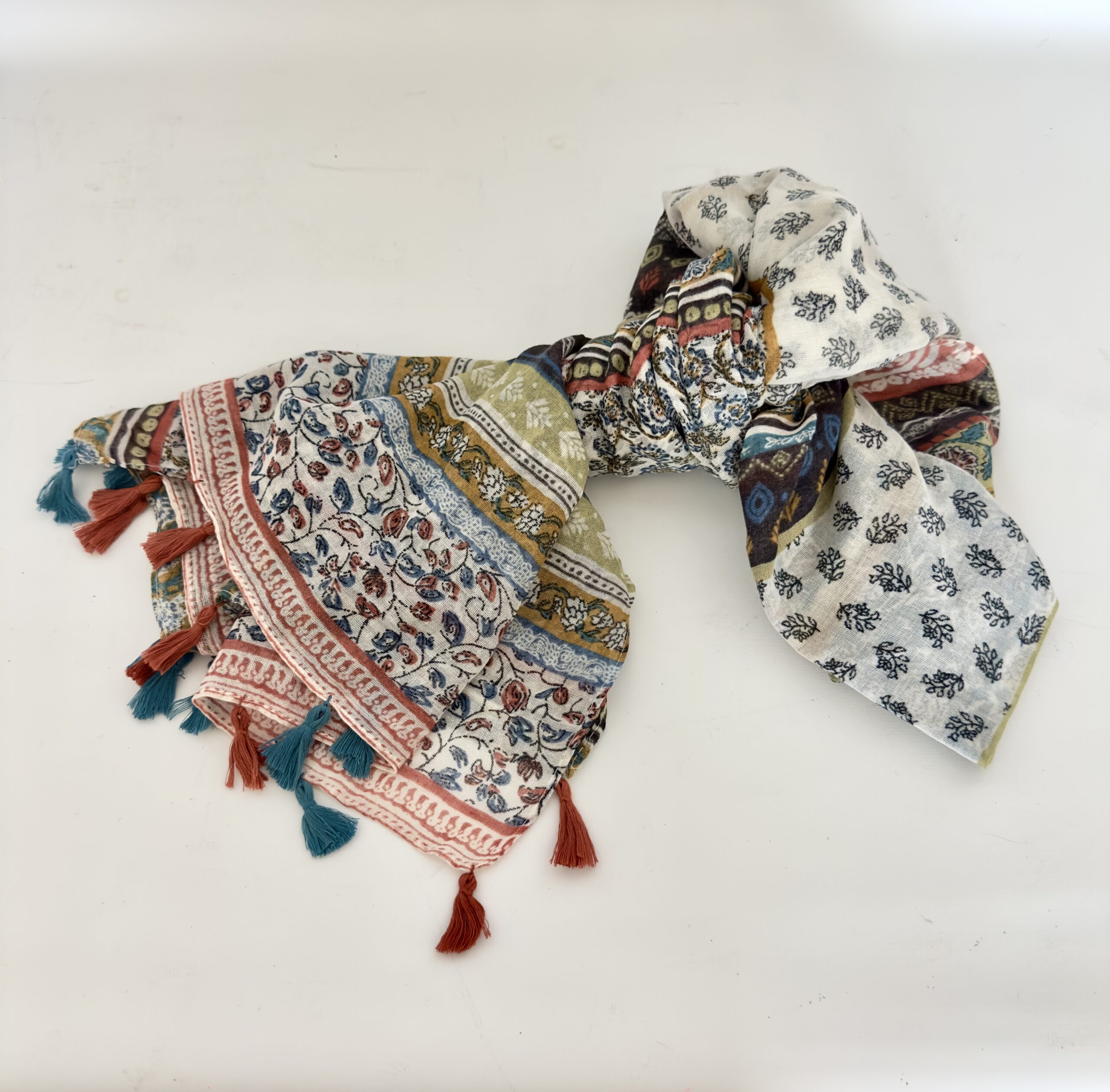 Lightweight cream scarf with a patchwork of floral prints, including a vine of blue and terracotta buds, a terracotta border, bands of mustard, sage green and navy, and a panel of small navy sprigs, finished with alternating teal and rust tassels.