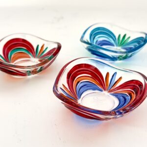 Small shallow glass dish with a wavy rim, decorated with bands of red, orange, yellow, green and blue radiating from the centre like flower petals.