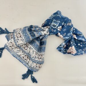 Lightweight scarf in denim blue with large blush pink, white and pale blue flowers, and ends bordered with bands of cream florals, navy medallions and dotted stripes, finished with clusters of blue tassels at the corners.