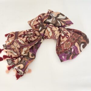 Lightweight scarf printed with large swirling florals and medallions in peach, plum purple, burgundy, chocolate brown and cream, finished with alternating burgundy and peach tassels.