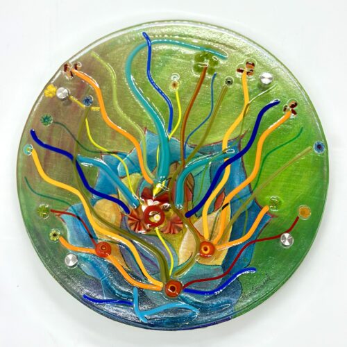 A circular glass piece with beautiful blue and green designs and acrylic-painted canvas beneath